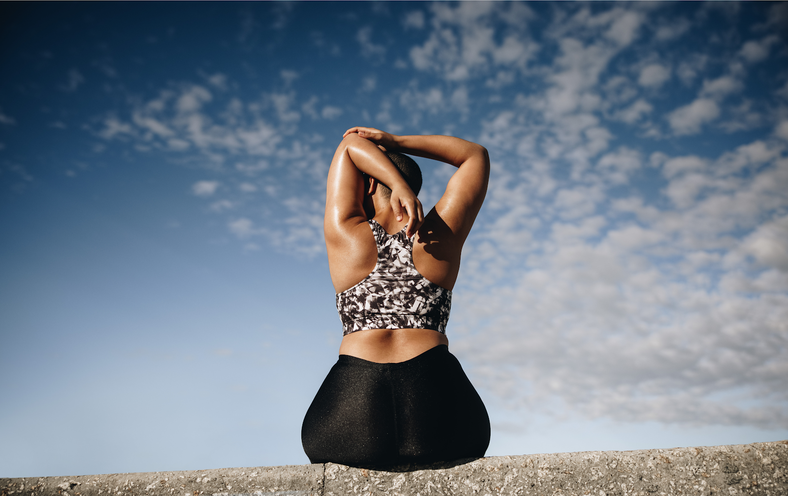 Woman in sports bra and leggings sitting on wall