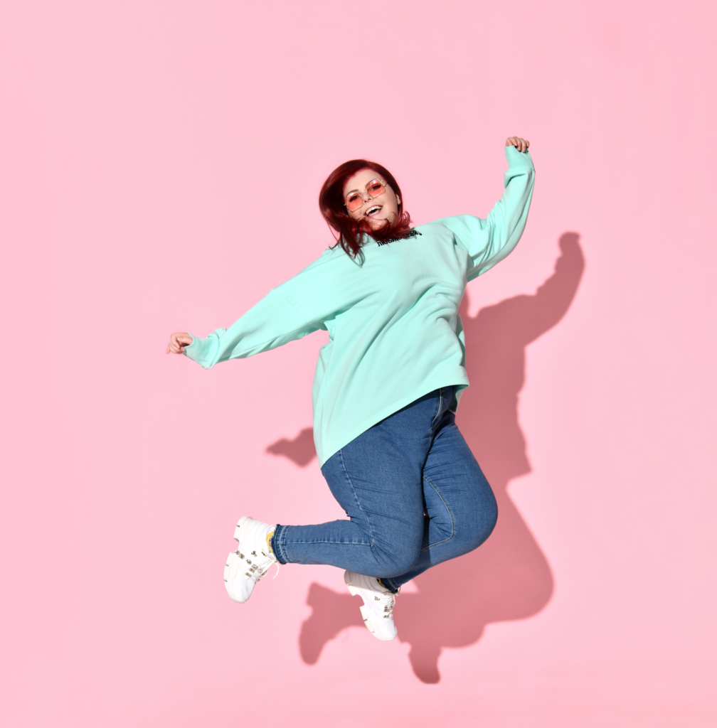Woman in a light blue sweater jumping in front of a pink background